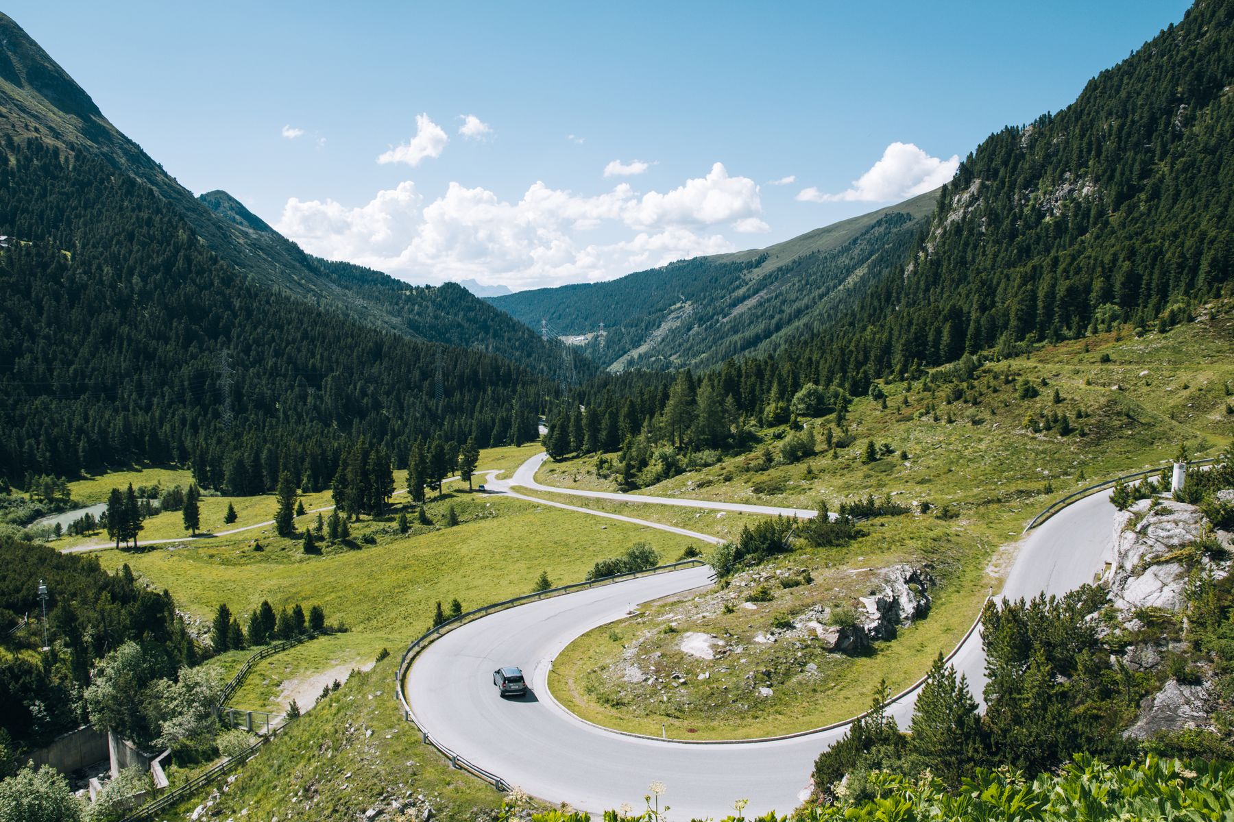 Graue Passstraße zwischen grünen Berghängen in Tirol